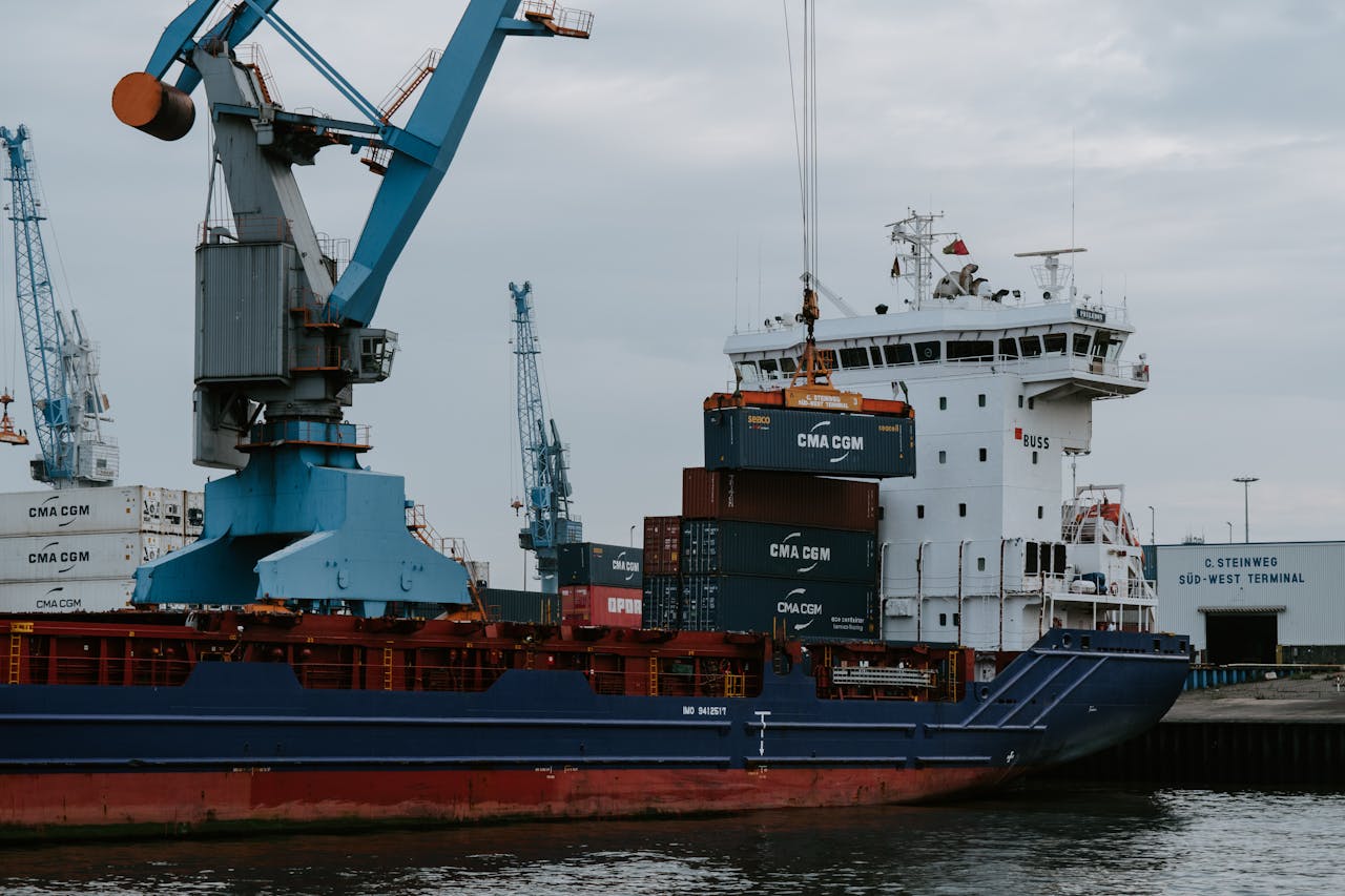 A cargo ship loaded with shipping containers at an industrial harbor with cranes.