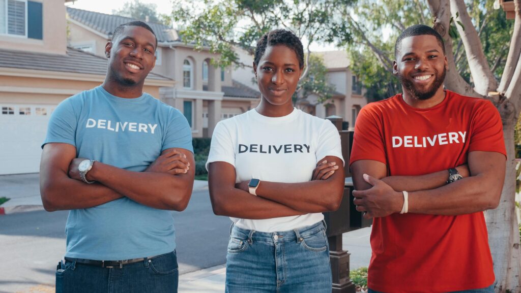 Cheerful delivery team standing outdoors with confident smiles, wearing matching delivery shirts.